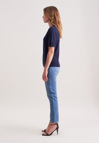 Granatowa koszulka z krótkim rękawem o okrągłym dekolcie, w zestawie z jasnoniebieskimi dopasowanymi dżinsami, dopełniona czarnymi sandałkami na wysokim obcasie.