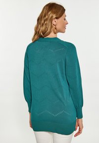 Zöldeskék, hosszú ujjú pulóver zig-zag mintával, nyitott mintázatú és bordázott mandzsettákkal, csípőig érő hosszúsággal.