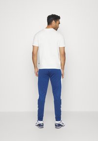 Vit kortärmad t-shirt i kombination med blåa träningsbyxor med vita sidosträck, smidig tyg och avslappnad passform. Bekväm och väldesignad för god andning.