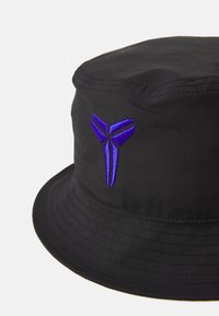 Chapeau seau noir fabriqué en tissu résistant, présentant un logo brodé violet bien en vue sur le côté. Large bord et texture lisse.