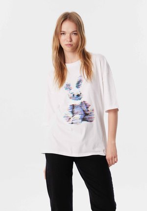 T-shirt oversize blanc présentant un graphique de lapin multicolore. Matière en coton doux avec des manches courtes et un col rond.