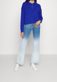 Polo a maniche lunghe a maglia blu, jeans a zampa di elefante in denim azzurro e sneakers bianche. Design semplice con contrasto tra i tessuti.