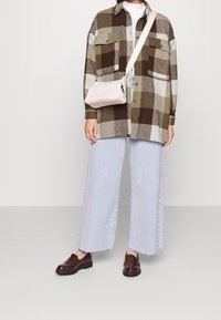 Ruudullinen paita ruskean ja vihreän sävyissä, vaaleat farkkushortit, ruskeat loafers-kengät ja pieni beigeläjäri.