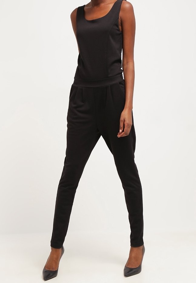 Haut noir sans manches et ajusté, associé à un pantalon noir taille haute fuselé et des escarpins noirs pointus sur une personne debout.