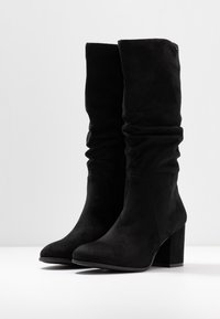 Svarta knähöga stövlar i mjukt mocka, med en slappa design och fyrkantiga klackar. Ytan verkar slät utan synligt hårdvara.