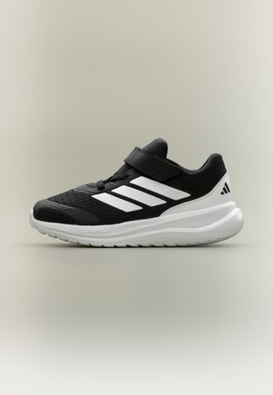 Baskets athlétiques noir et blanc avec trois bandes blanches, fermeture velcro, semelle blanche rembourrée et tige en mesh respirant, présentées sur un fond pâle.