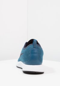 Modrá sportovní obuv s perforovaným svrchním materiálem z semiše, elegantním designem, černo-bílou gumovou podrážkou a kontrastním zadním panelem.