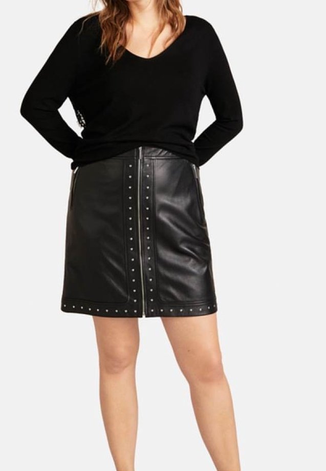 Sort lædernederdel med naglede accenter og en frontlynlås. Matcher med en sort langærmet top med v-udskæring.