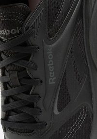 Chaussure de sport noire en matériau mesh et synthétique, avec un système de laçage proéminent et un logo Reebok sur le côté.