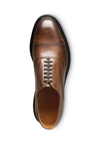 Chaussure en cuir marron avec un embout arrondi, un laçage, des coutures détaillées et une semelle noire texturée. L'intérieur présente le logo de la marque.
