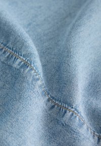 Tessuto azzurro chiaro con una texture liscia, caratterizzato da cuciture visibili lungo i bordi. La superficie mostra lievi segni di usura e una delicata lucentezza.