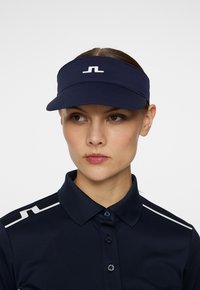 Marinblå skärm med lättviktsmaterial, prydd med en vit logotyp, designad med en böjd skärm och ett justerbart band bak.