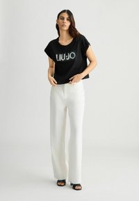 Crop top noir avec le logo "LIU-JO" en strass ; associé à un pantalon large blanc et des sandales à talons noires. Textures lisses et coupe décontractée.