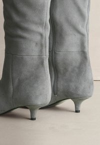 Gray suede ankle boots with a slim heel, featuring a visible black zipper along the back and smooth, textured surface.