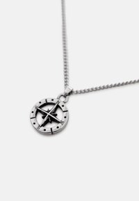 Pendentif boussole en argent avec des marquages directionnels sur une chaîne, présenté sur un fond blanc uni.