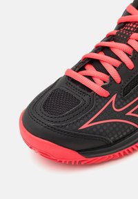 Scarpa sportiva nera con lacci e suola rosa brillante. Presenta pannelli in rete testurizzati e un design a pois sul materiale.