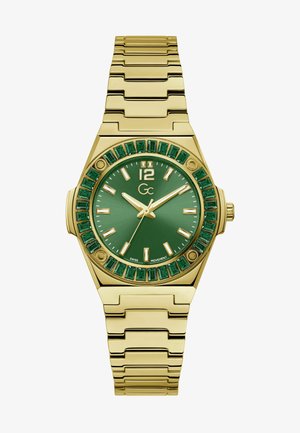 Guldfarvet armbåndsur med en grøn urskive, smaragdformede accenter omkring bezel'en og et metalkædearmbånd. Har hvide timemarkører.