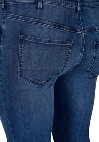 Tamno plave traperice s uskim krojem, dva stražnja džepa i suptilnom teksturom. Materijal je mekan s vidljivim detaljima šivanja.