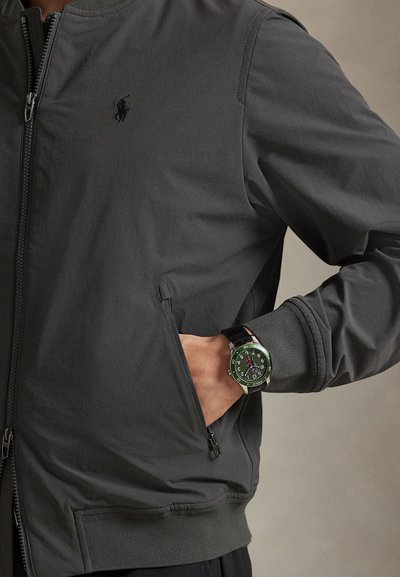 Meeste tumehall bomberjakk, millel on esiosal tõmblukk, soonikservad ja küljetaskud. Kandke selle juurde musta ja rohelise nahkrihmaga kella.