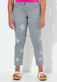 Šedé džíny s frayed aplikacemi ve tvaru hvězdy, slim fit, střední pas a zkrácená délka. V kombinaci s bílými platformovými sandály.