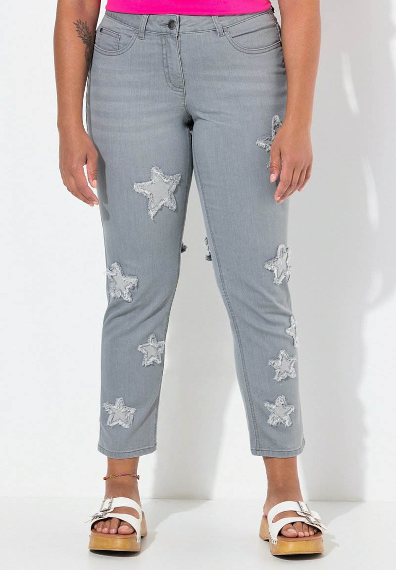 Šedé džíny s frayed aplikacemi ve tvaru hvězdy, slim fit, střední pas a zkrácená délka. V kombinaci s bílými platformovými sandály.