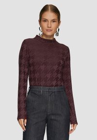 Langsleeve, hoge hals top in donker bordeaux met houndstooth patroon, gecombineerd met donkere hoge taille broeken. Glad stoftextuur.