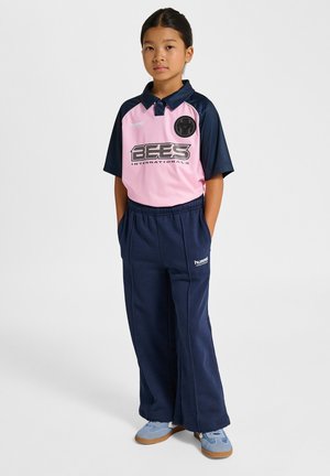 Lyserød og marineblå træningsdragt med korte ærmer og logo, med krave og elastik i taljen. Blå sko fuldender outfittet.