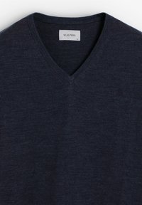 Pulover dintr-un amestec de lână de culoare bleumarin, cu guler în V, textură fină și un logo discret brodat pe piept. Etichetă vizibilă care indică marca și mărimea.