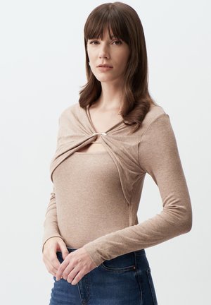 Bruine langarmige top met een geknoopte voorkant en een zilverkleurige accent. De stof lijkt zacht en geribbeld, gedragen met denim.