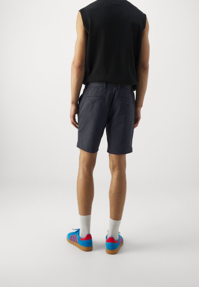 Pantaloni corti grigi scuri da uomo, con tasche e una vestibilità comoda, abbinati a vivaci sneaker blu con dettagli rosa e calze bianche.