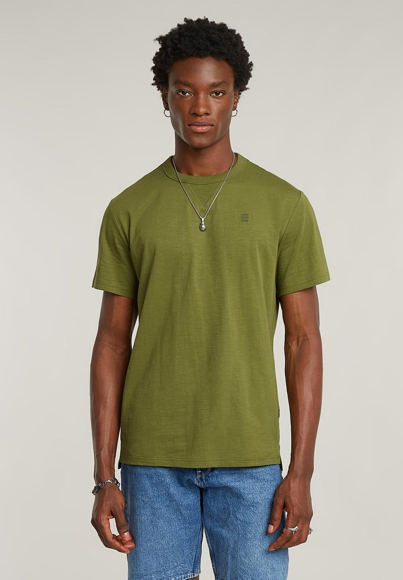 T-shirt in cotone verde oliva con scollo tondo e maniche corte; presenta un piccolo dettaglio con logo sul petto. Abbinata a pantaloncini di jeans.