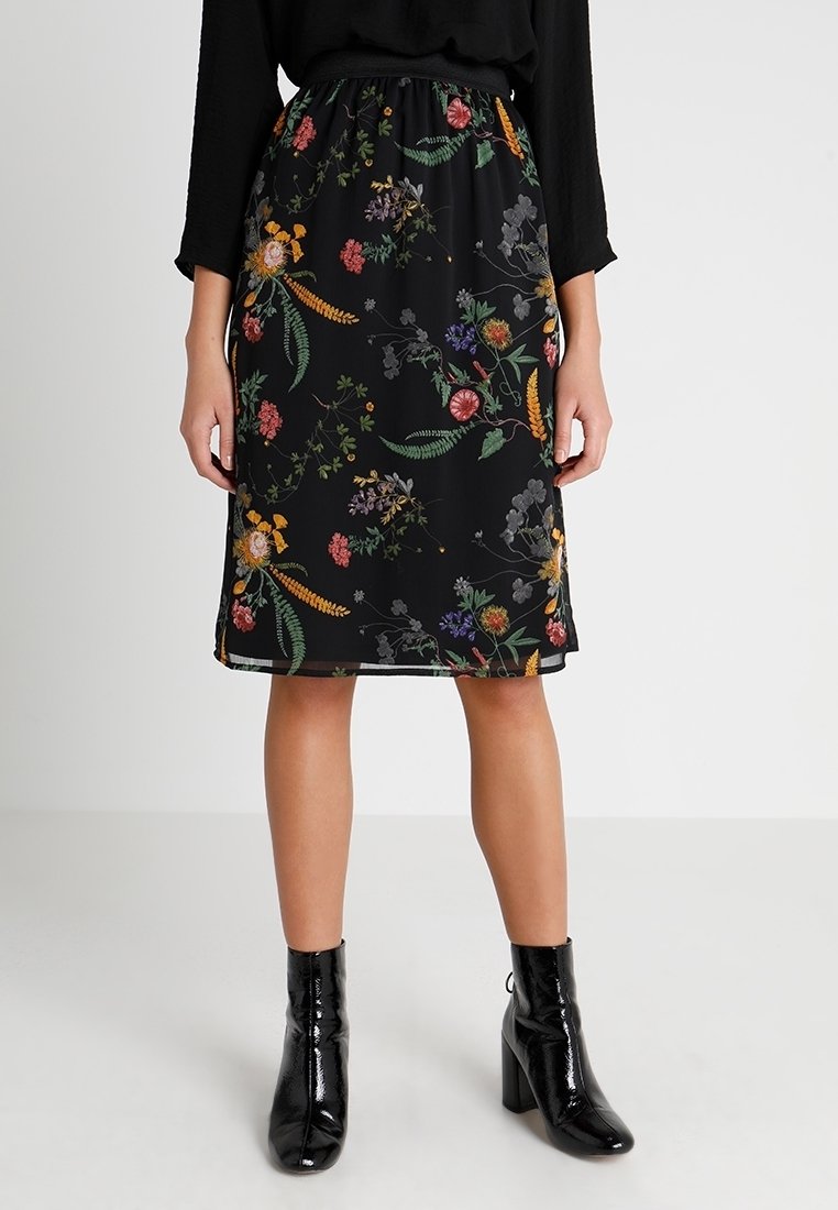 Jupe noire avec un motif floral de différentes couleurs. Taille élastique, design à mi-mollet et tissu léger. Bottines noires brillantes.
