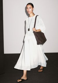 Weißes Strickoberteil, fließender weißer Rock mit horizontalen Streifen, dunkle gewebte Handtasche und schwarze Flip-Flops. Einfaches und minimalistisches Design.