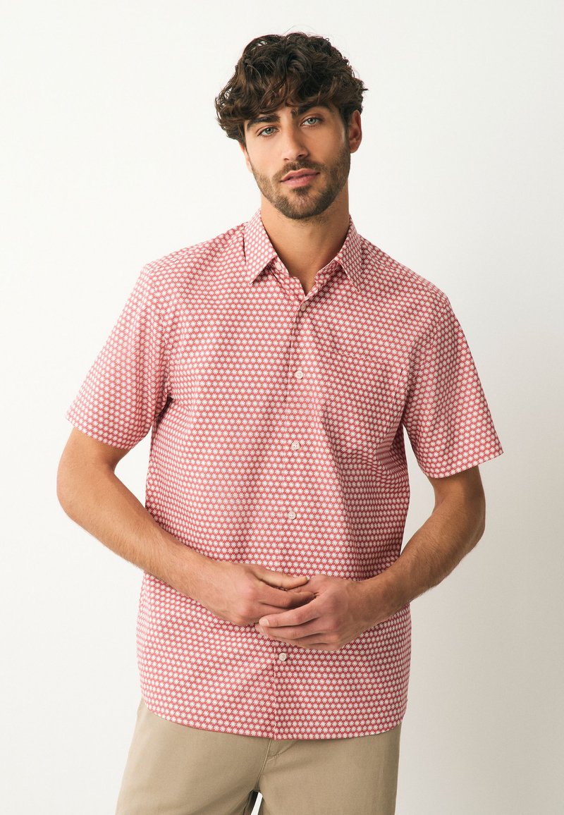 Chemise à manches courtes avec boutons, rouge à motif floral blanc. Fabriquée en tissu léger, avec un col classique et une coupe droite.