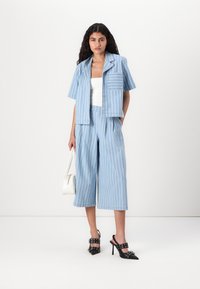 Blå- og hvitstripet kort jakke med korte ermer, kombinert med løse stripete culottes. Modellen holder en hvit håndveske og har på seg svarte hæler.