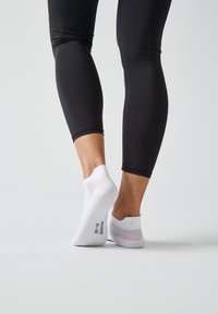 Witte enkelkousen van ademend mesh bij de hiel, gecombineerd met zwarte nauwsluitende leggings, die een gladde en rekbare stof tonen.
