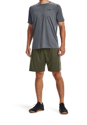 Grijze sport T-shirt met korte mouwen, gecombineerd met olijfgroene shorts en zwarte sportschoenen met een gestructureerde zool.