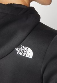 Black hooded jacket in smooth fabric, featuring a white logo on the shoulder, with a close-up view of the collar and sleeve details.