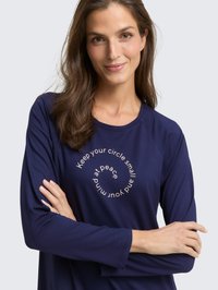 Tamsiai mėlyna marškinėlių su ilgomis rankovėmis, apvalios apykaklės ir šviesios spalvos užrašais. Minkšta medžiaga, laisvas kirpimas ir raglaninės rankovės.