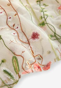 Tissu transparent avec des fleurs délicates et des vignes brodées en tons verts, rouges, orange et blanc sur un fond clair.