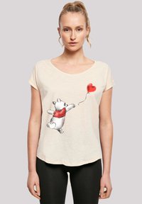 Cream-colored T-shirt featuring a cartoon bear in a red sweater, reaching for a red heart balloon. Soft, casual fabric with relaxed fit.