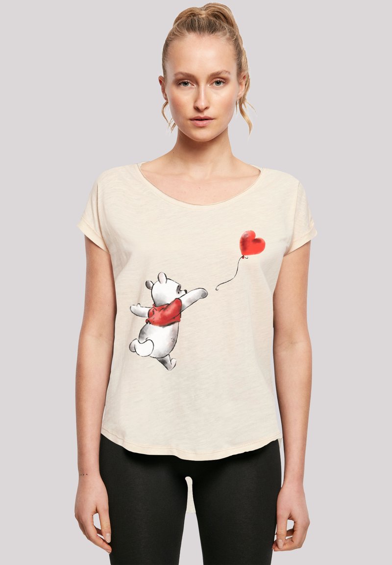 Cream-colored T-shirt featuring a cartoon bear in a red sweater, reaching for a red heart balloon. Soft, casual fabric with relaxed fit.