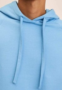 Felpa blu chiaro con lacci indossata da una persona, che mostra il décolleté e la parte superiore del petto su uno sfondo neutro.