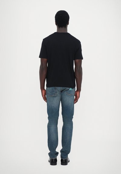 T-shirt noir à manches courtes associé à un jean bleu délavé moyen. Le jean présente un design classique à cinq poches et des coutures discrètes.