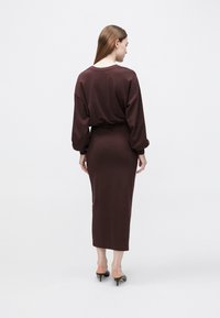 Długa bordowa sukienka z długimi rękawami i dopasowaną talią. Wykonana z miękkiego materiału, z dekoltem w łódeczkę i prostą sylwetką.