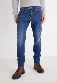 Kék farmernadrág, slim fit fazonnal, öt zsebbel, fém gombos záródással és finom gyűrődéssel a combokon.