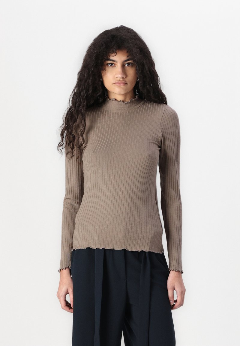 Ribbed brown long-sleeve top with a mock neck and uneven scalloped hem. Soft texture, fitted design, and elongated sleeves.