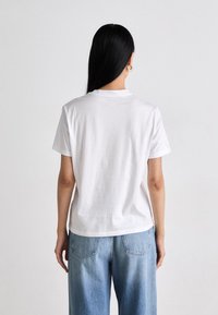 Hvit bomull t-skjorte med korte ermer og rund hals, med en avslappet passform. Kombinert med lyseblå, litt for store denimjeans.