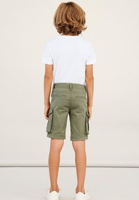 Khaki cargo shorts with side pockets, cotton fabric, and a relaxed fit. Paired with a white short-sleeve t-shirt and white shoes.