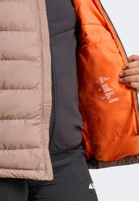 Lekka kurtka puchowa z beżową zewnętrzną warstwą, ciemnoszarymi bokami i jasnopomarańczowym wnętrzem. Posiada zamek błyskawiczny i widoczną metkę pielęgnacyjną wewnątrz.